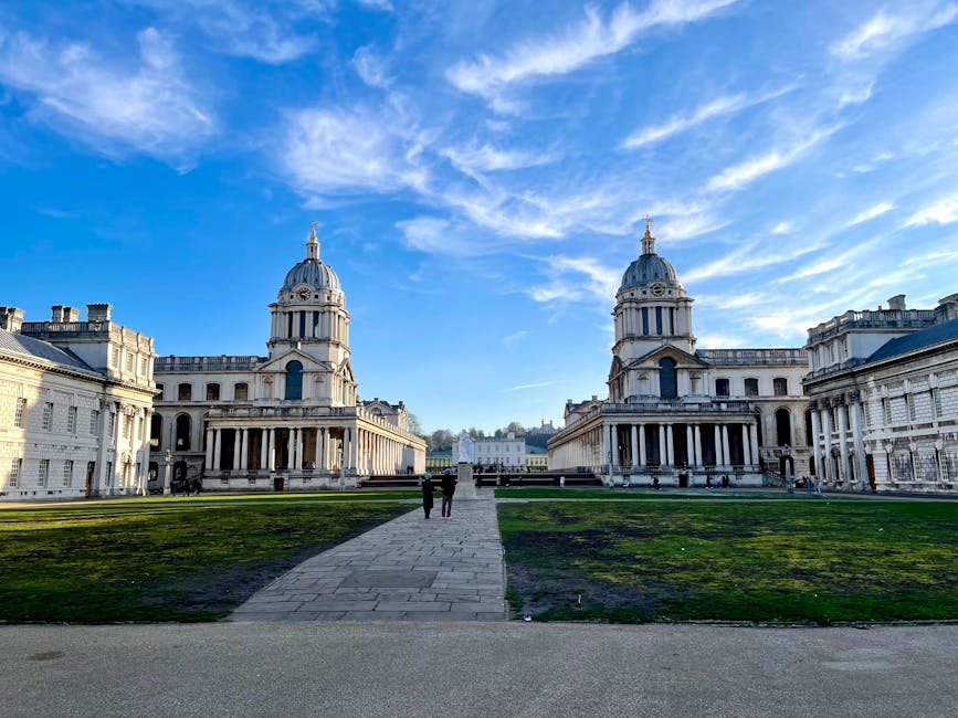 A wide view of a historic neoclassical building with two prominent domed towers, set against a bright blue sky with wispy clouds. The building’s façade features large columns and detailed stonework, with a central pathway leading up to it. In the foreground, a pavement area is visible, and a few people are walking along the stone pathway toward the entrance. The surrounding area includes grassy lawns and a paved walkway, with some individuals near the building’s steps. This scene exemplifies a well-maintained public or cultural site, with ample open space suitable for visitor access or events, and the image highlights the building’s architectural features and the clear weather conditions typical of a pleasant day, potentially supporting house removals or relocation planning visits.